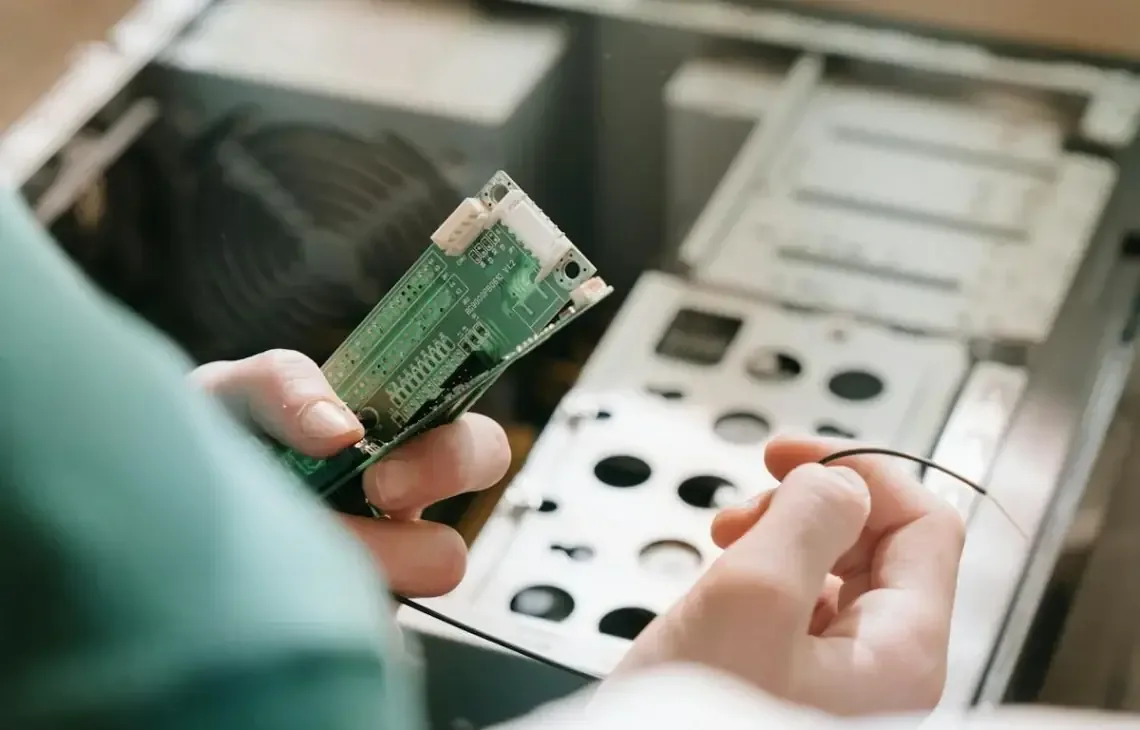 Dłonie serwisanta z płytką elektroniczną nad otwartą obudową komputera stacjonarnego