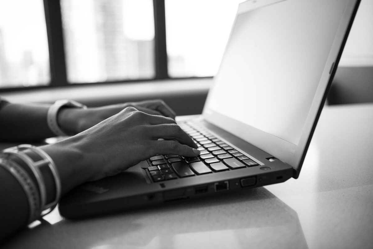 Dłonie piszące na klawiaturze laptopa przy oknie