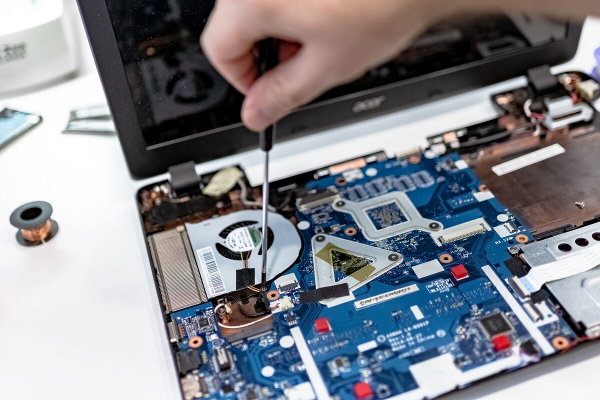 Dłoń z wkrętakiem przy płycie głównej otwartego laptopa podczas naprawy
